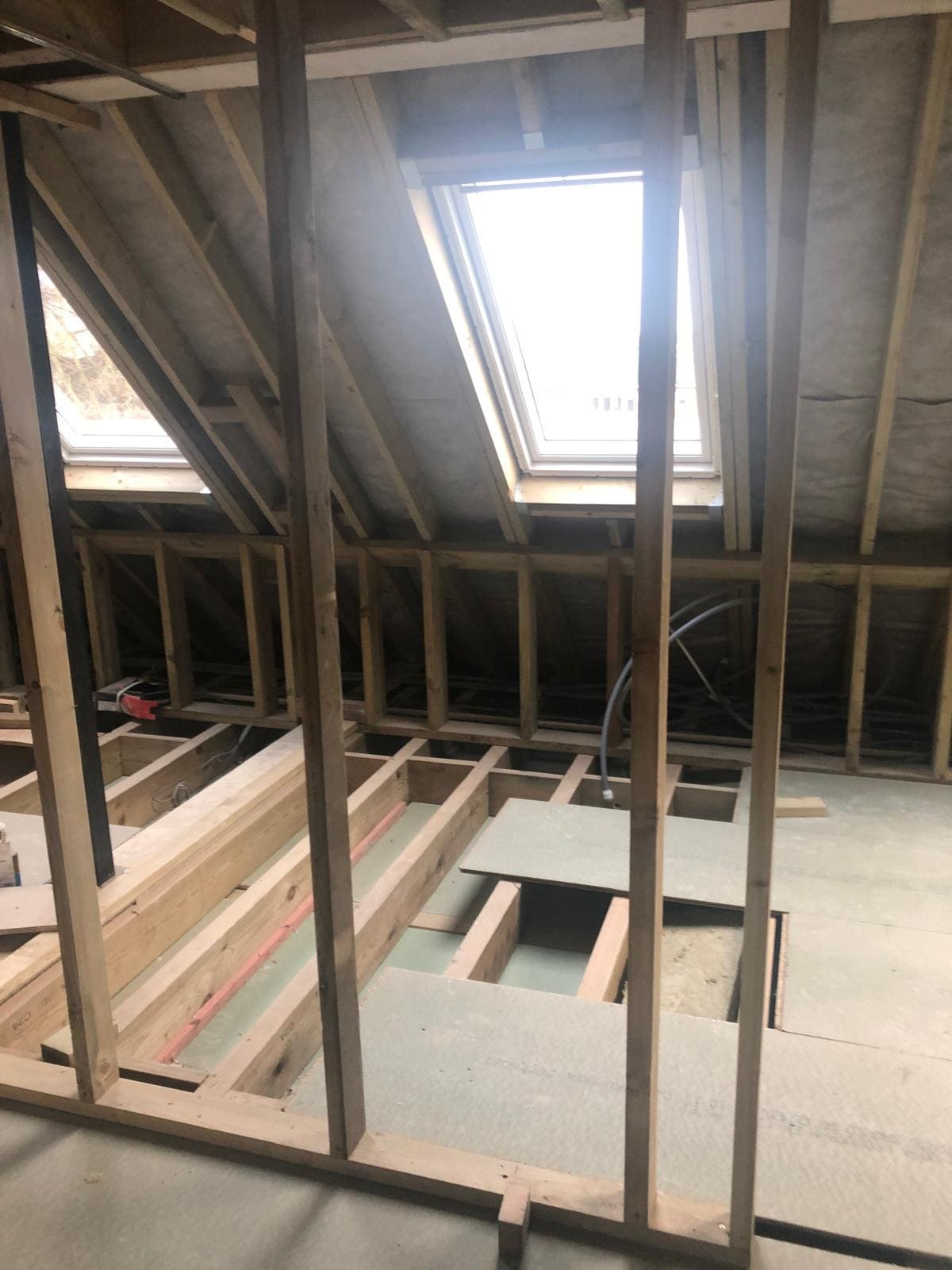 Loft conversion mid-build in a London property showing new stud framing, joists and a Velux roof window fitted by Refurb Squad
