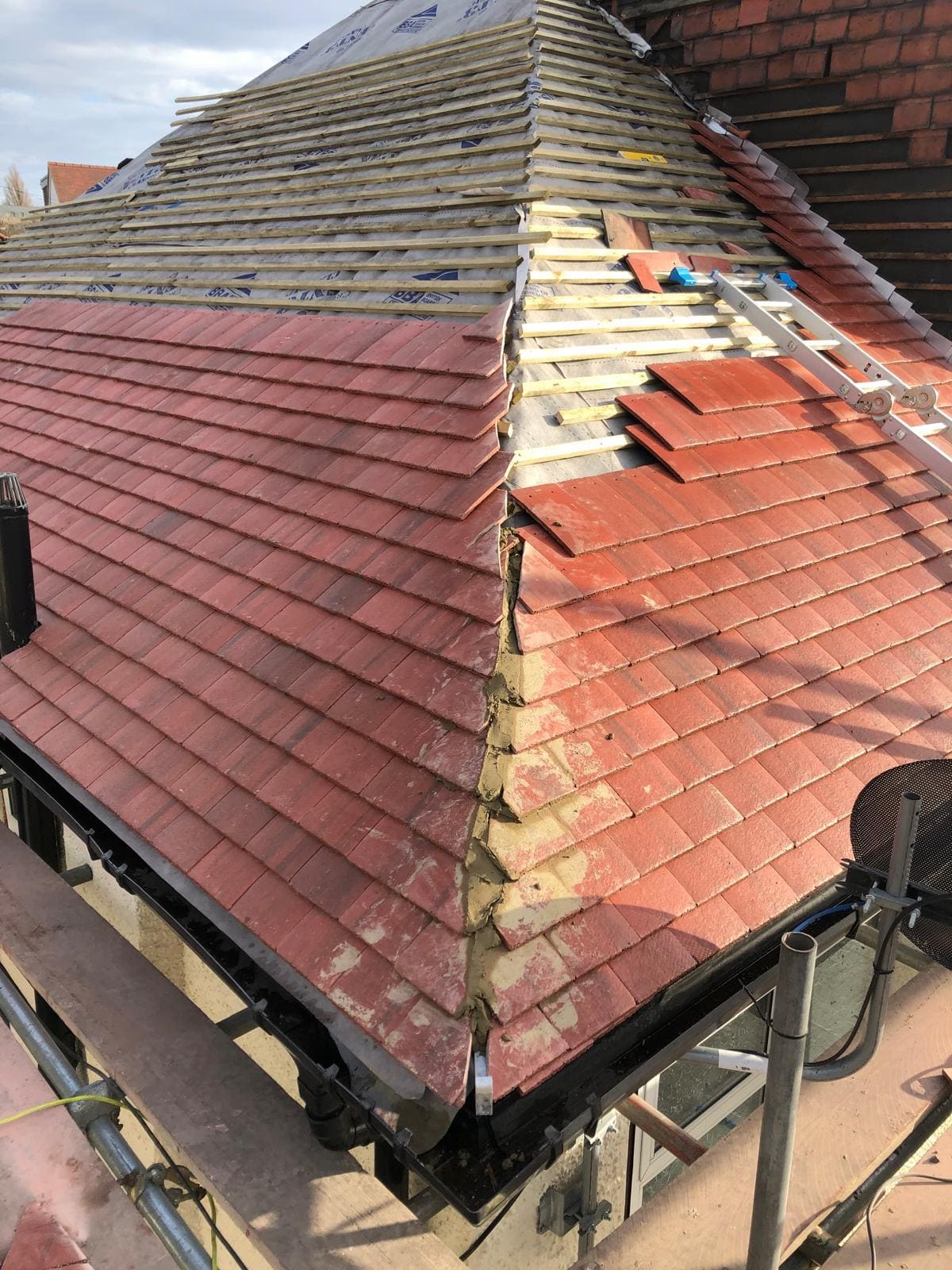 London hip roof re-tile in progress showing new red clay tiles, mortar bedding and roofing membrane by Refurb Squad