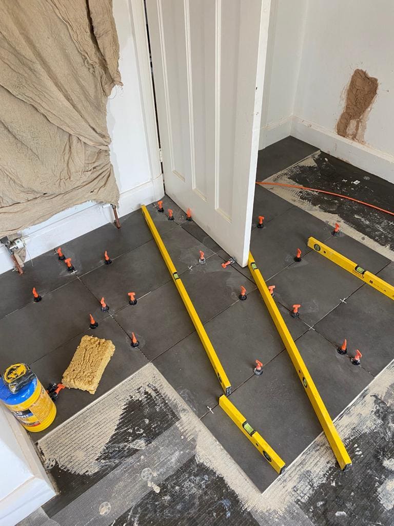 Large-format porcelain floor tiles being laid with levelling clips in a London kitchen installation